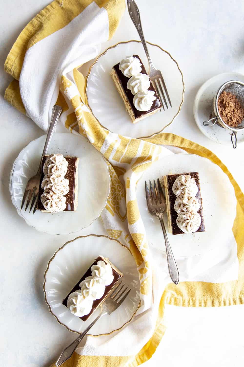 Rediscover an old fashioned icebox cake with layers of graham crackers, pudding and frosting in this amazing Chocolate Eclair Dessert. The different layers and textures will make your mouth so happy. Four slices of cake on white plates.