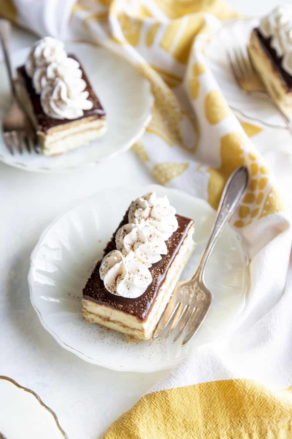 Rediscover an old fashioned icebox cake with layers of graham crackers, pudding and frosting in this amazing Chocolate Eclair Dessert. The different layers and textures will make your mouth so happy. Eclair cakes on white plates with forks.