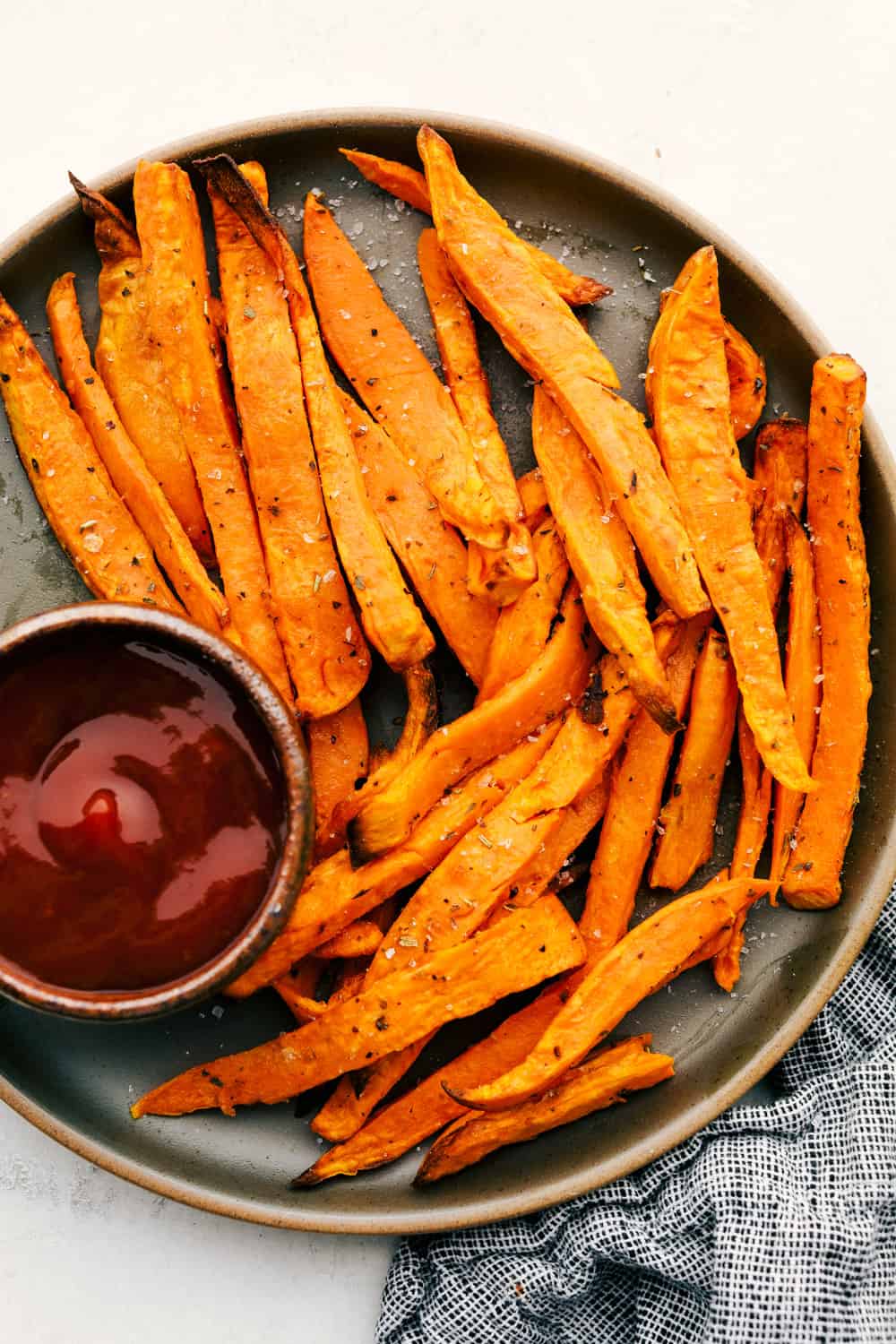 Perfect Air Fryer Sweet Potato Fries are crispy outside and tender inside. Lightly seasoned and golden, they are a delicious addition to any meal. These are a healthy way to indulge without the guilt. Pair them with your favorite dipping sauce and your side dish is done! Sweet potato fries on a plate with sauce for dipping.