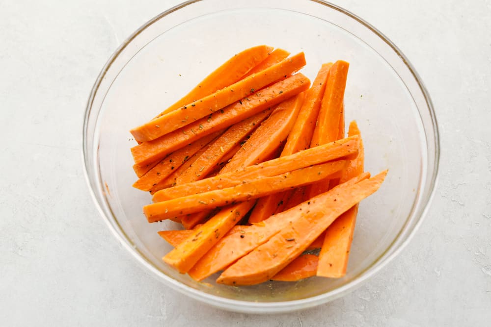 Perfect Air Fryer Sweet Potato Fries are crispy outside and tender inside. Lightly seasoned and golden, they are a delicious addition to any meal. These are a healthy way to indulge without the guilt. Pair them with your favorite dipping sauce and your side dish is done! Covering the sweet potato fries with oil and seasonings.