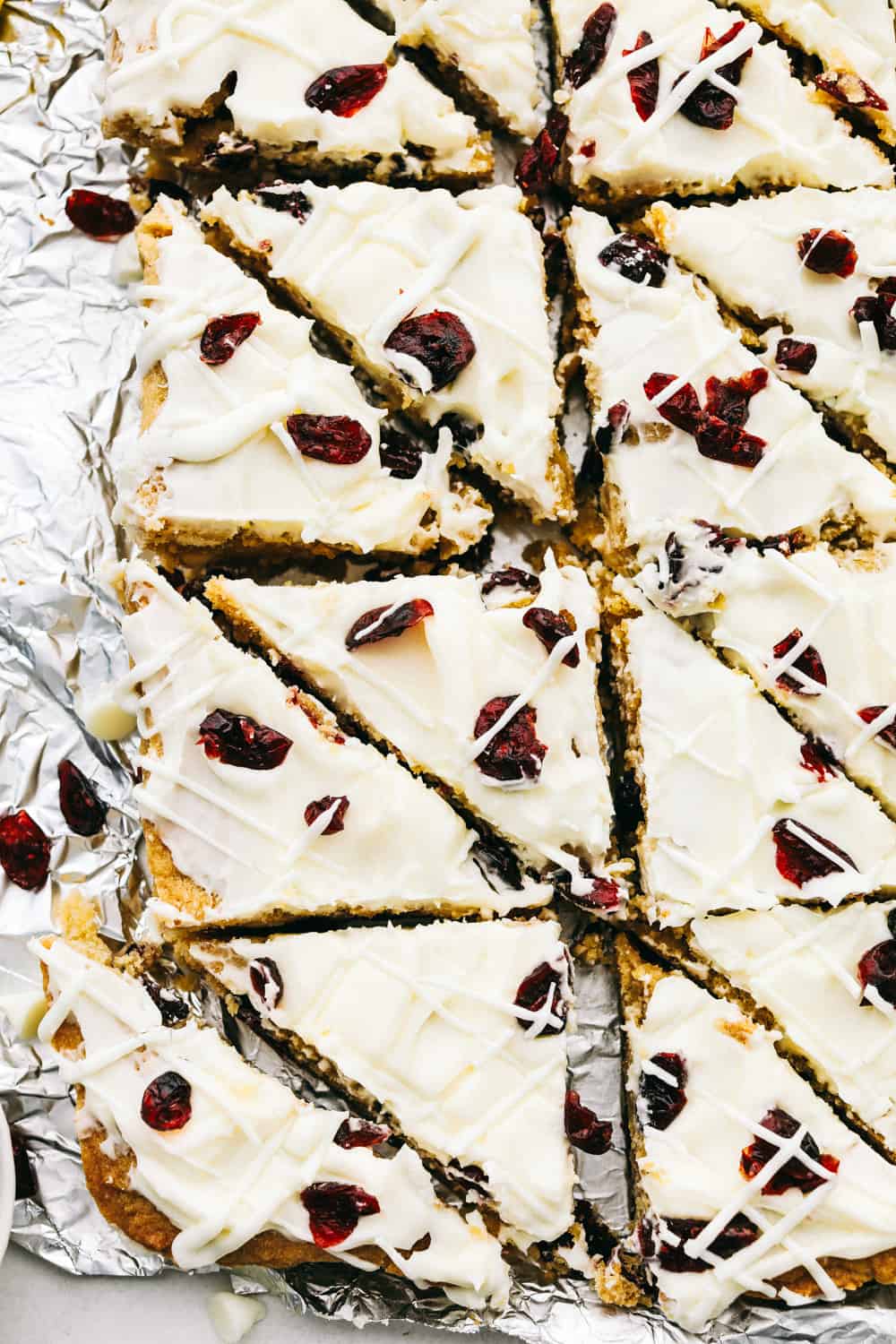 These Cranberry Bliss Bars are a little slice of heaven! White chocolate chips hidden in a blondie cookie bar with dried cranberries then the perfect cream cheese frosting overtop and finished off with sprinkled droplets of cranberries and a white chocolate drizzle for the best garnish is just the beginning! Cut cranberry bliss bars in triangles.