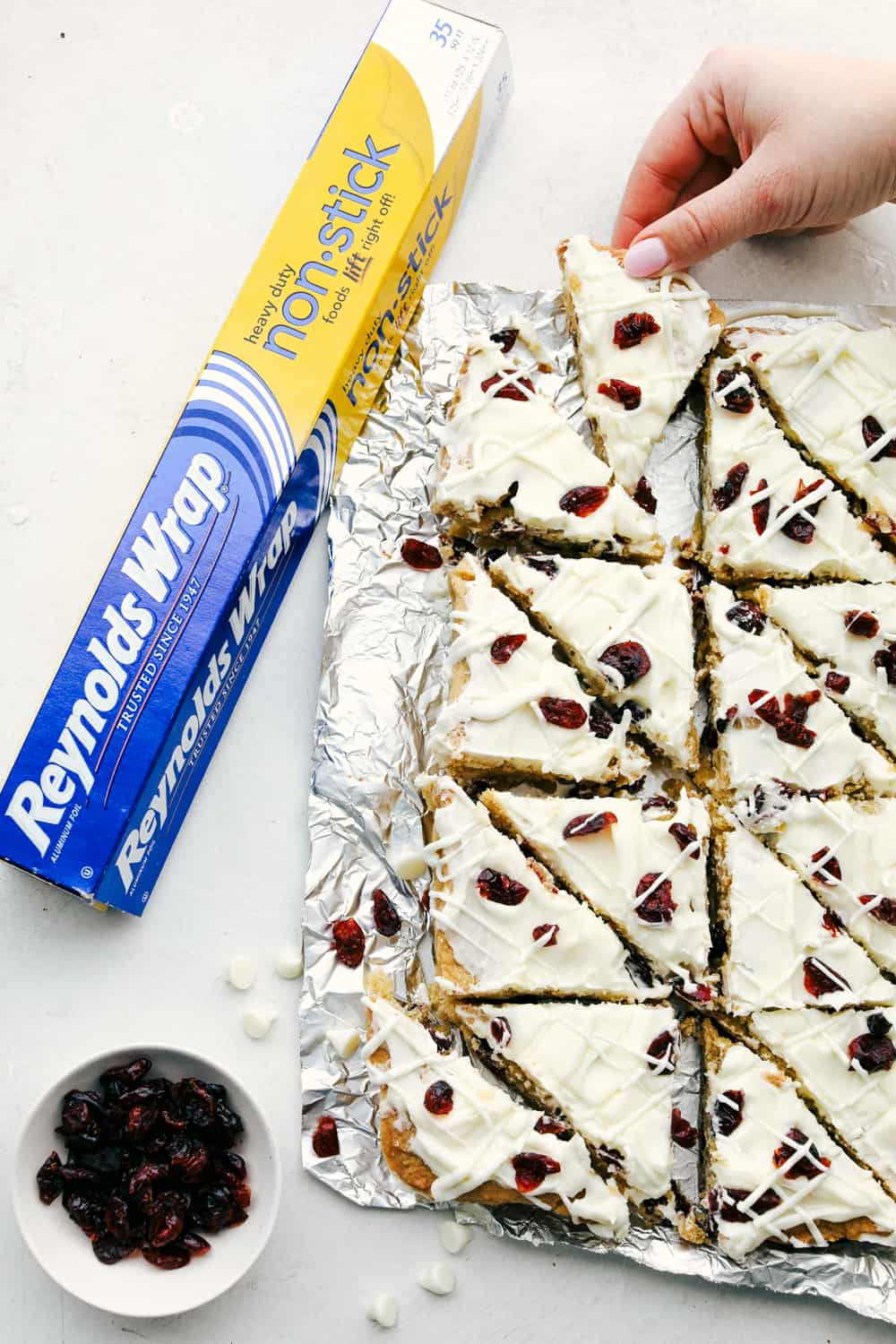 These Cranberry Bliss Bars are a little slice of heaven! White chocolate chips hidden in a blondie cookie bar with dried cranberries then the perfect cream cheese frosting overtop and finished off with sprinkled droplets of cranberries and a white chocolate drizzle for the best garnish is just the beginning! Cranberry bliss bars cut into triangles.