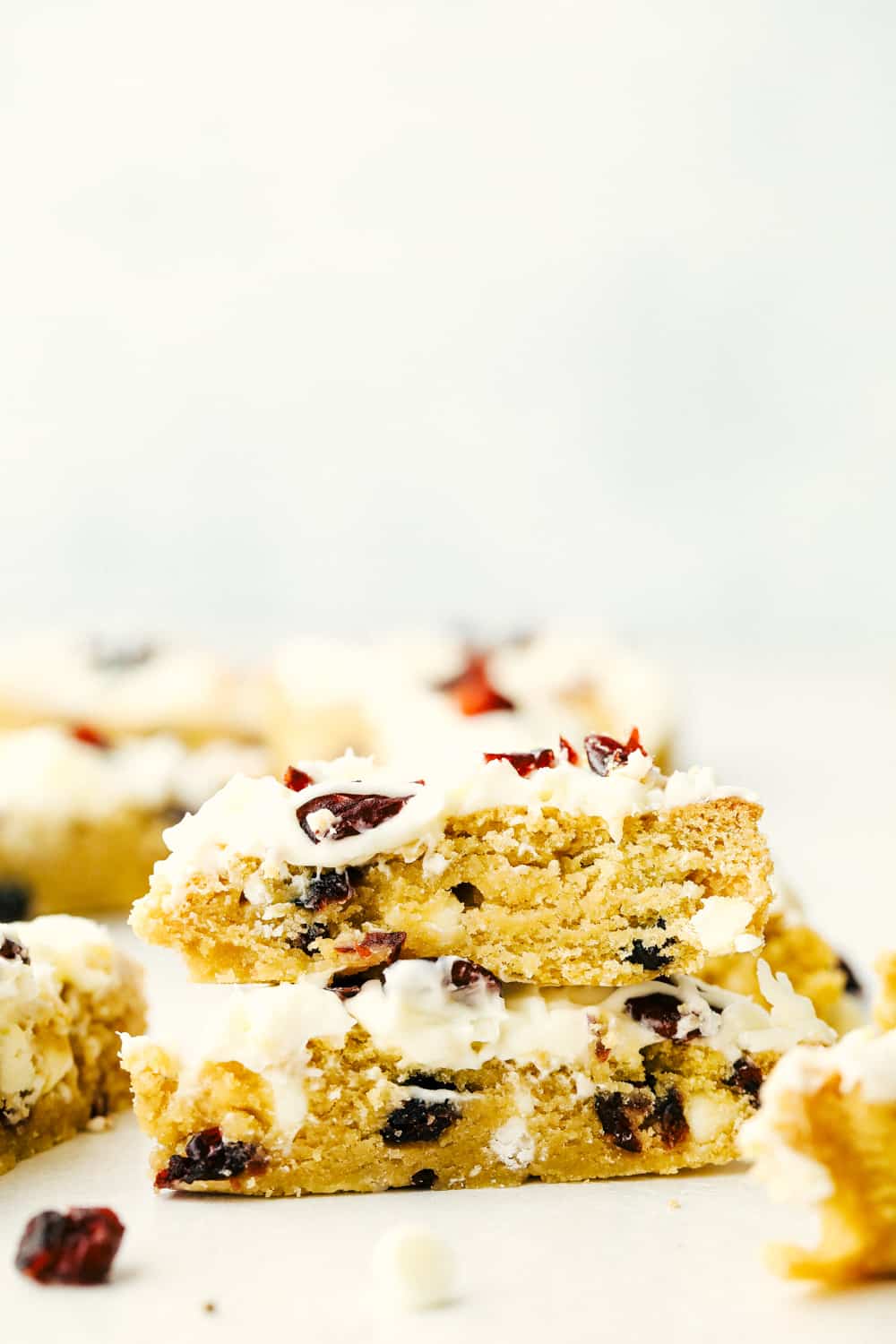 These Cranberry Bliss Bars are a little slice of heaven! White chocolate chips hidden in a blondie cookie bar with dried cranberries then the perfect cream cheese frosting overtop and finished off with sprinkled droplets of cranberries and a white chocolate drizzle for the best garnish is just the beginning! Cranberry bliss bars stacked on top of each other.