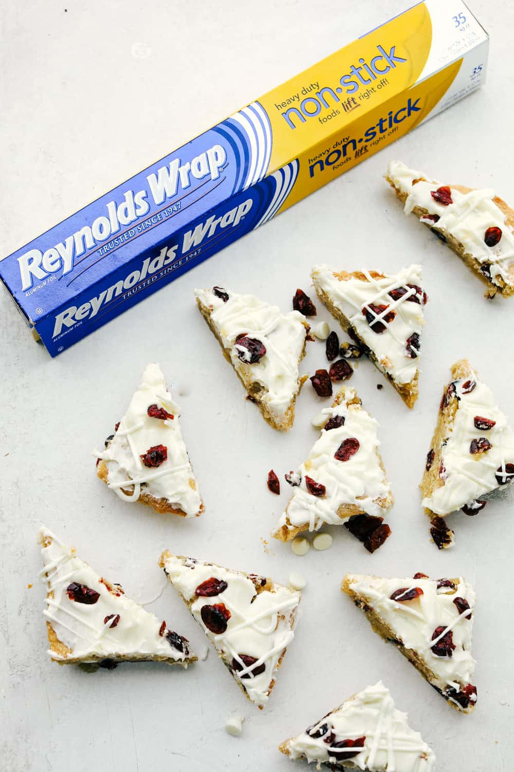 These Cranberry Bliss Bars are a little slice of heaven! White chocolate chips hidden in a blondie cookie bar with dried cranberries then the perfect cream cheese frosting overtop and finished off with sprinkled droplets of cranberries and a white chocolate drizzle for the best garnish is just the beginning! Cranberry bliss bars cut into triangles spread apart.