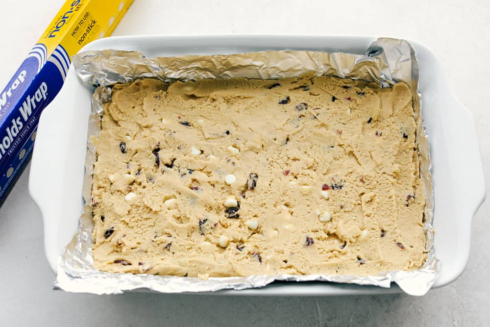 These Cranberry Bliss Bars are a little slice of heaven! White chocolate chips hidden in a blondie cookie bar with dried cranberries then the perfect cream cheese frosting overtop and finished off with sprinkled droplets of cranberries and a white chocolate drizzle for the best garnish is just the beginning! The dough is in the baking dish.
