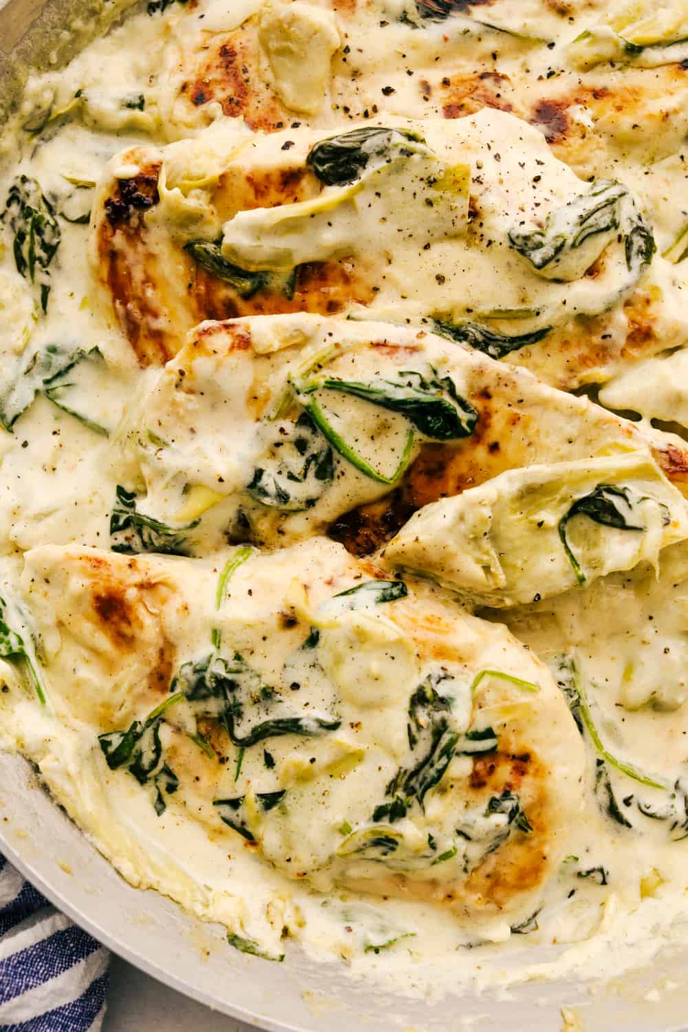 Pan seared chicken is smothered in a decadent sauce with spinach and artichokes in this Creamy Spinach Artichoke Chicken. It's a quick simple way to put a gourmet meal on the table any day of the week. Not only is it quick to make, it's made all in one pot so clean up is a breeze. Saucy spinach artichoke chicken on a plate.