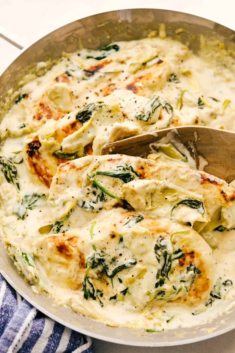 Pan seared chicken is smothered in a decadent sauce with spinach and artichokes in this Creamy Spinach Artichoke Chicken. It's a quick simple way to put a gourmet meal on the table any day of the week. Not only is it quick to make, it's made all in one pot so clean up is a breeze. Spooning chicken with spinach artichoke in a creamy sauce.