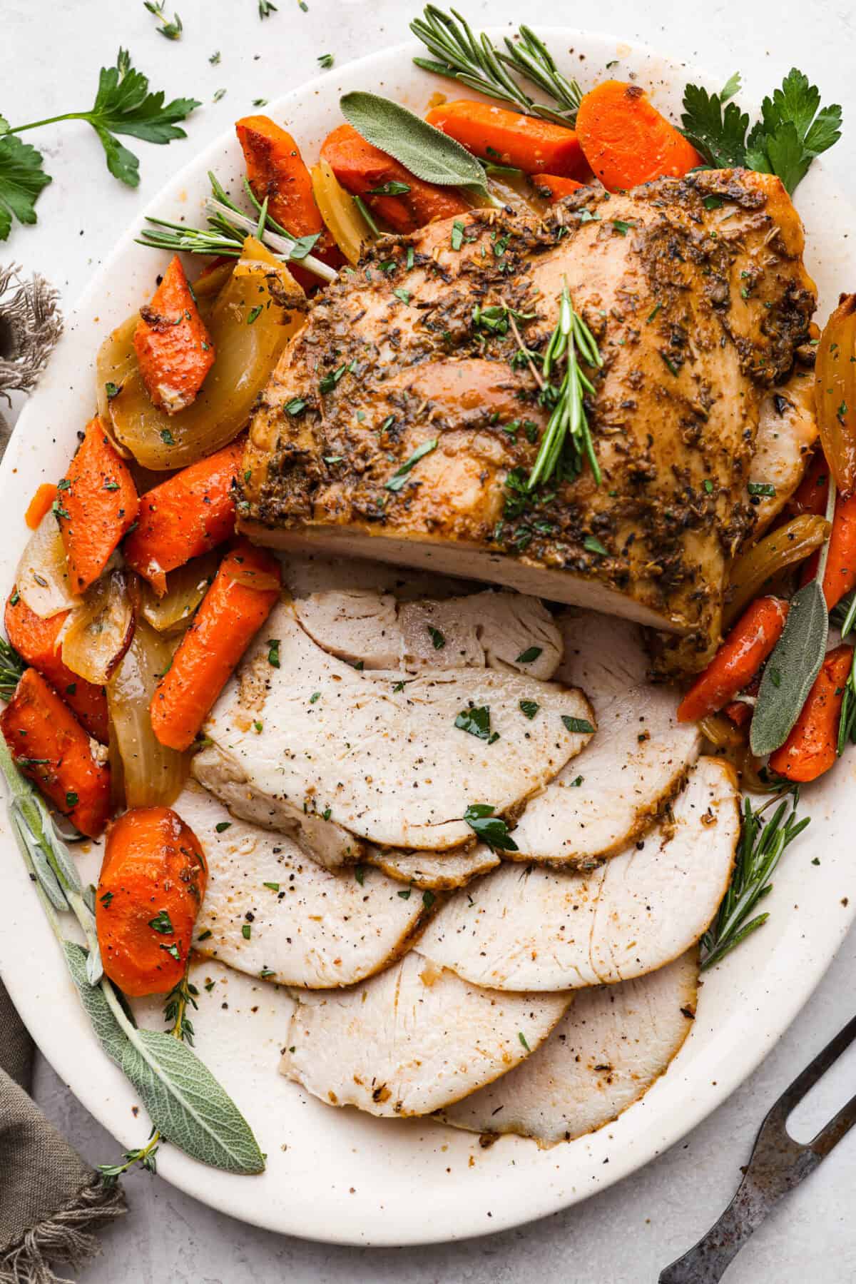Slow Cooker Turkey Breast is the perfect way to get tender, juicy turkey with a fraction of the prep but all the flavor. Let the slow cooker do ALL the work! Overhead shot of a platter with the vegetables and slow cooker turkey breast with fresh herbs.