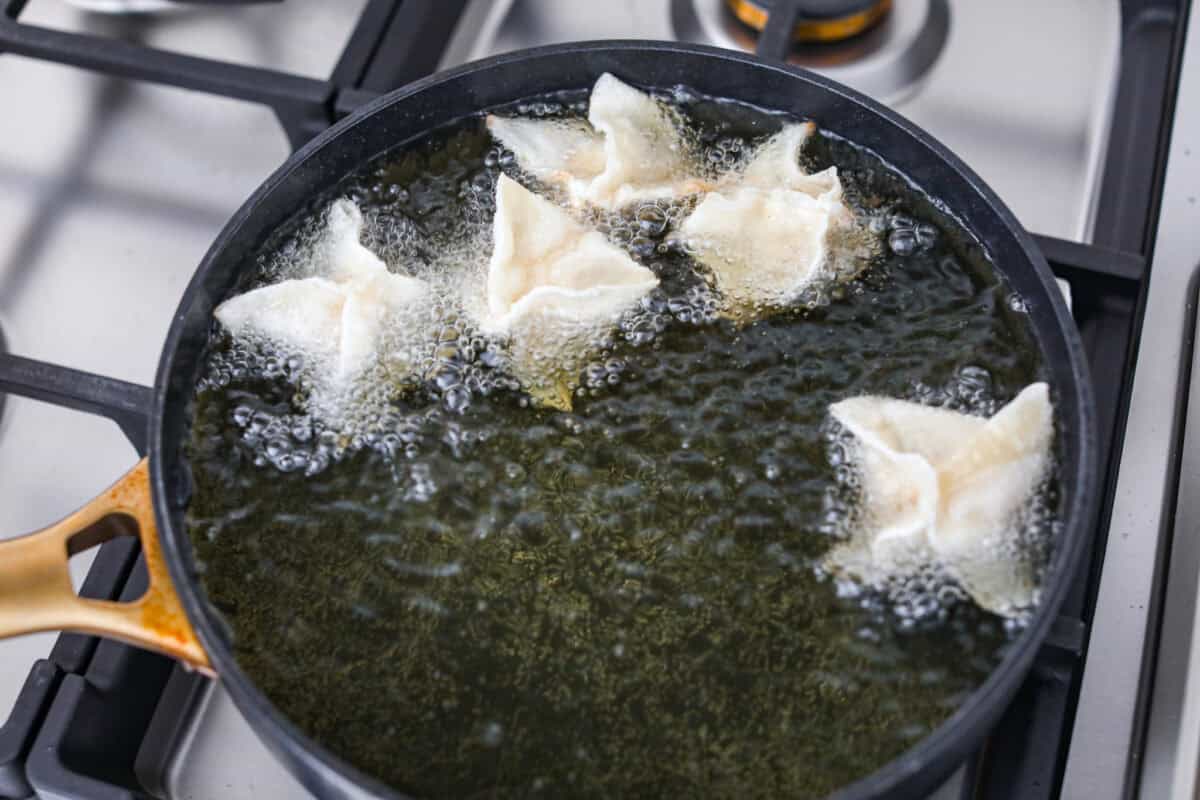 Crab Rangoons are a fun, Asian-inspired appetizer filled with crab meat, smooth cream cheese, and seasoning. Wrapped in a wonton wrapper and deep-fried, they are irresistible! Overhead shot of sealed crab rangoon in oil frying.