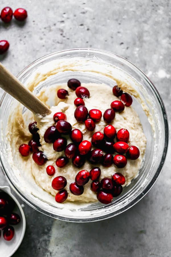These Cranberry Muffins are the perfect blend of tart and sweet, light, fluffy and perfect for your morning breakfast. All you need is one bowl and 30 minutes to whip these babies up from start to finish. Muffin batter in a glass bowl with cranberries on top.