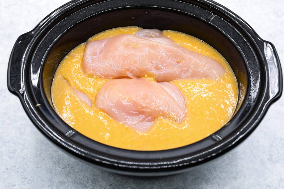 Slow-cooker creamy chicken and broccoli over rice is a super easy, delicious meal the whole family will love! Moist chicken and tender broccoli combine in a cheesy sauce that's absolutely divine.ย Overhead shot of sauce with chicken breasts on top in crockpot.