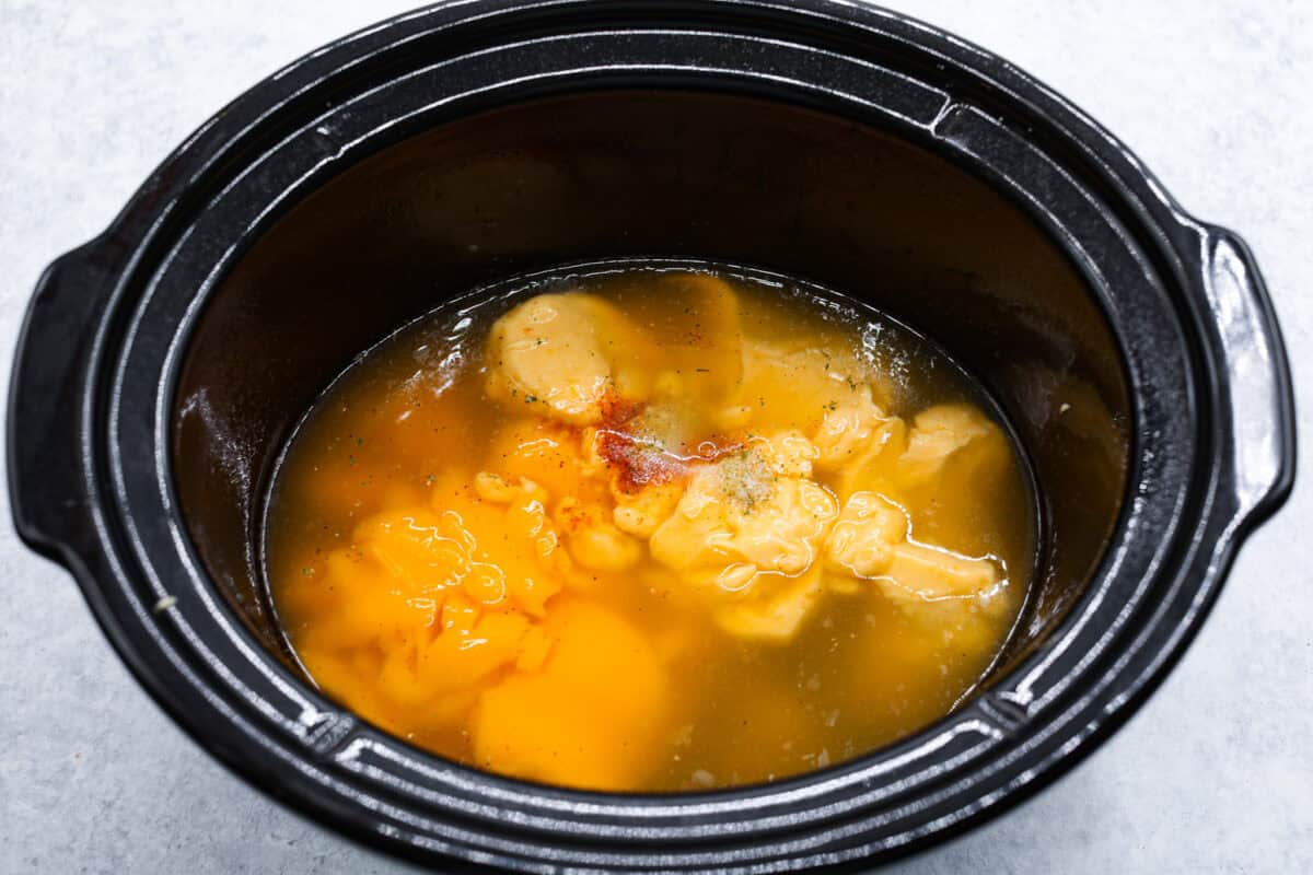 Slow-cooker creamy chicken and broccoli over rice is a super easy, delicious meal the whole family will love! Moist chicken and tender broccoli combine in a cheesy sauce that's absolutely divine.ย Overhead shot of soups, broth and seasonings in the bottom of a crockpot.