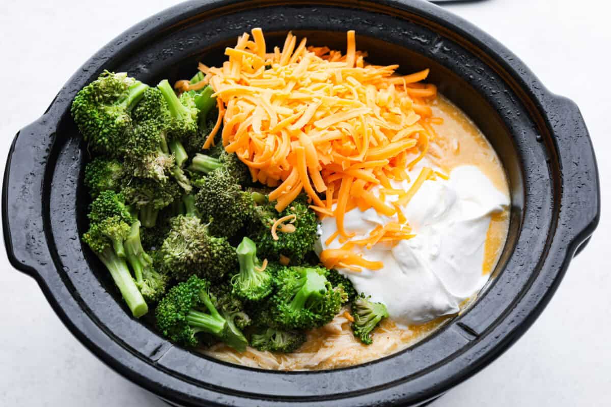 Slow-cooker creamy chicken and broccoli over rice is a super easy, delicious meal the whole family will love! Moist chicken and tender broccoli combine in a cheesy sauce that's absolutely divine.ย Overhead shot of broccoli, cheese and sour cream over the top of the chicken mixture.