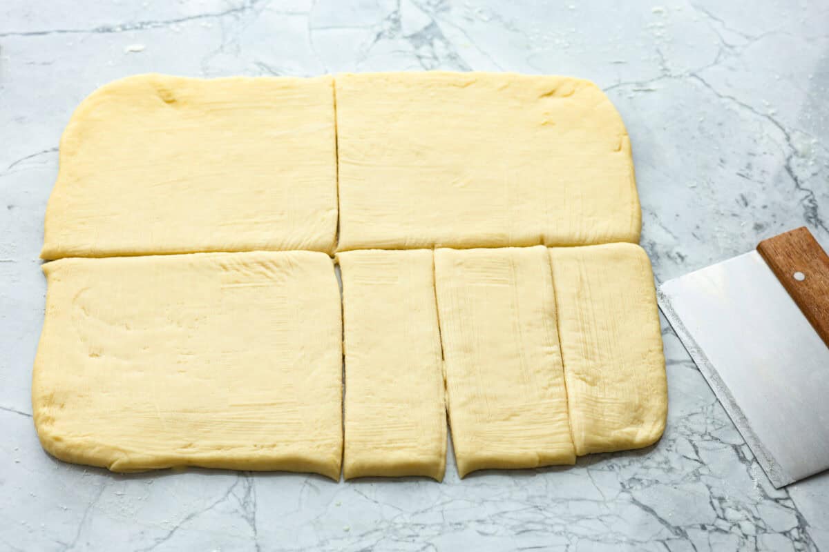 Lion House Rolls are the best dinner rolls for holiday meals or any occasion. These buttery, super-soft rolls are the perfect vehicle for soaking up delicious soups, sauces, and gravies. Overhead shot of rectangular dough cut into fourths and then one of the fourth cut into thirds.