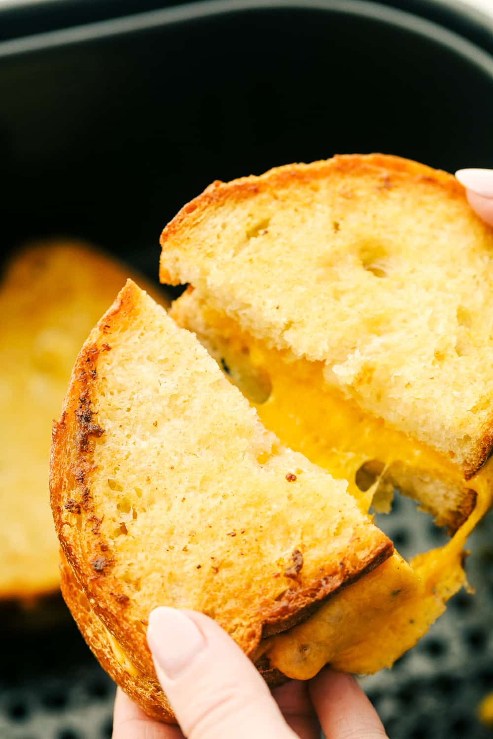 I want to introduce you to Air Fryer Grilled Cheese, the best I have ever had! Perfectly grilled to a crunchy golden brown on the outside and melty goodness on the inside. It's life changing. Close up shot of someone pulling the two parts of the sandwich apart to see the melty cheese.