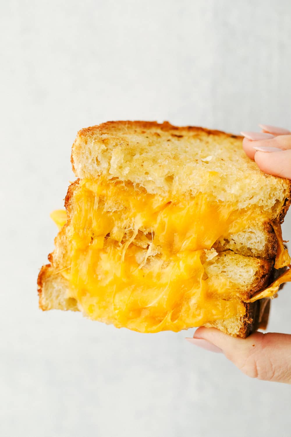 I want to introduce you to Air Fryer Grilled Cheese, the best I have ever had! Perfectly grilled to a crunchy golden brown on the outside and melty goodness on the inside. It's life changing. Holding a grilled cheese done in the air fryer cut in half.