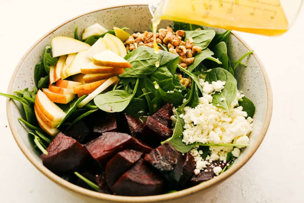 This Amazing Pear and Beet Salad is fresh, zingy, and absolutely delicious. It's a perfect combination of crisp-tender pears, sweet roasted beets, mixed greens all tossed in a honey vinaigrette. Pouring dressing over the bowl of salad.