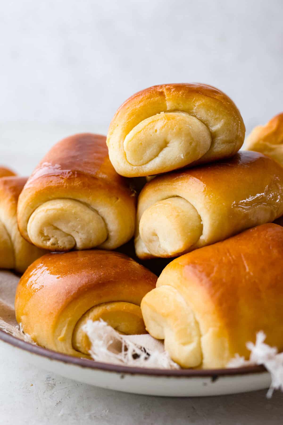 Lion House Rolls are the best dinner rolls for holiday meals or any occasion. These buttery, super-soft rolls are the perfect vehicle for soaking up delicious soups, sauces, and gravies. Angle shot of stacked lion house rolls.