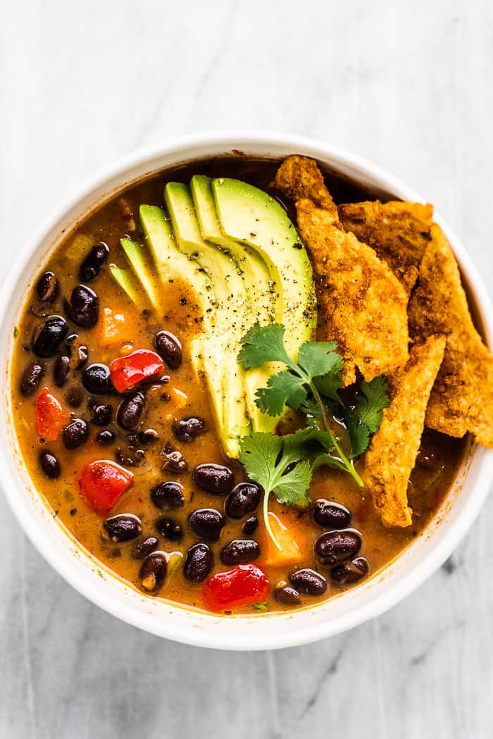 Black bean soup is easy to make, delicious, and healthy. It's made with kitchen-staples like cans of black beans, carrots, onions, and spices so you can make this recipe anytime you're craving Tex-Mex flavors. Black bean soup in a white bowl with avocado on top.