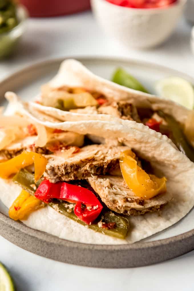 Mexican dinner night is fun and easy with these Crockpot Chicken Fajitas! They are loaded with chicken, bell peppers, onion, and spices, then served with all your favorite toppings. Crockpot chicken fajitas on tortillas on a plate.