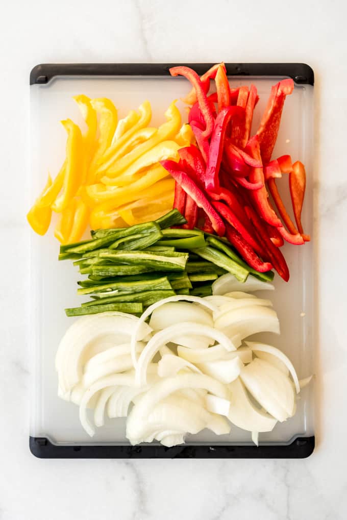 Mexican dinner night is fun and easy with these Crockpot Chicken Fajitas! They are loaded with chicken, bell peppers, onion, and spices, then served with all your favorite toppings. Sliced bell peppers and onions on a cutting board.