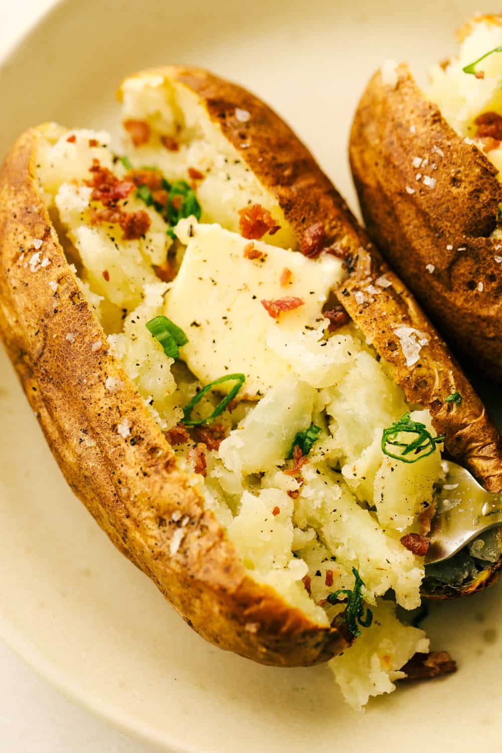 Perfect Air Fryer Baked Potatoes are crispy on the outside and tender fluffy on the inside. Perfect addition to any meal, or a meal all on it's own! Fluffy potatoes with butter, bacon and chives on a plate.