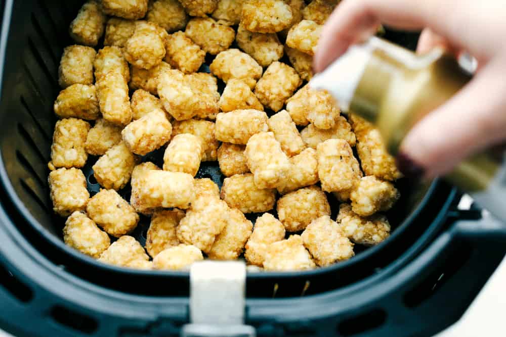 Air Fryer Tater Tots are just about the greatest thing to happen to potatoes ever! Crispy golden on the outside and tender on the inside, these are insanely delicious! Spraying olive oil on frozen tater tots in the air fryer.