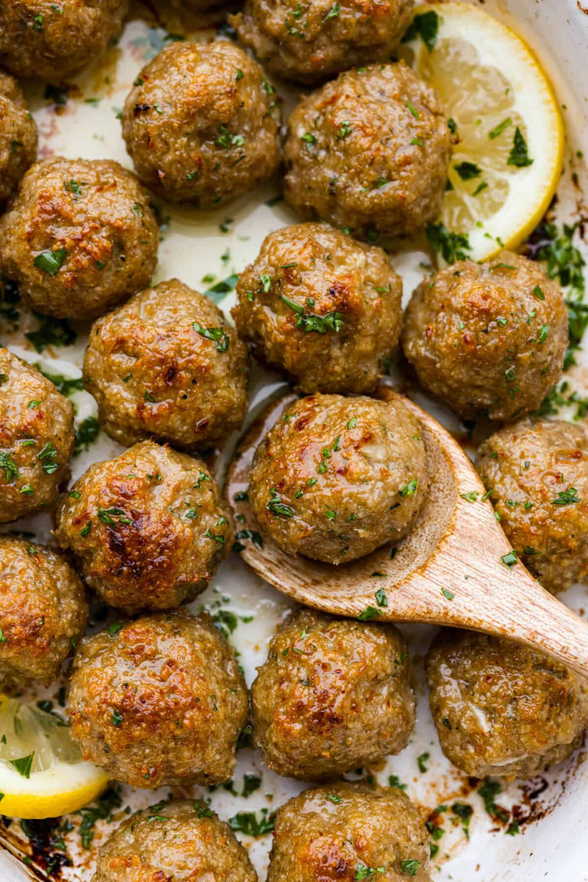 Baked Turkey Meatballs are tender, juicy, and perfectly seasoned. They're made with simple ingredients but big on flavor! These homemade meatballs are easy to make and healthy for the whole family! Close view of baked turkey meatballs in a baking dish with a wooden spoon lifting a meatball.
