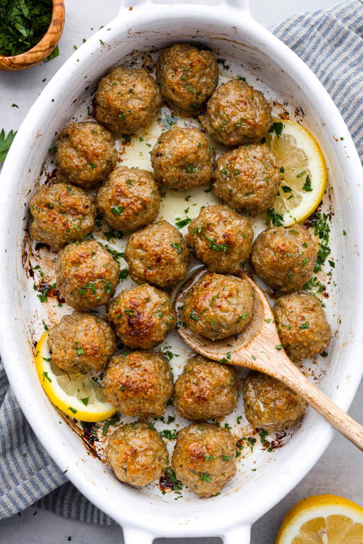 Baked Turkey Meatballs are tender, juicy, and perfectly seasoned. They're made with simple ingredients but big on flavor! These homemade meatballs are easy to make and healthy for the whole family! Top view of baked turkey meatballs in a white baking dish with a wooden spoon.