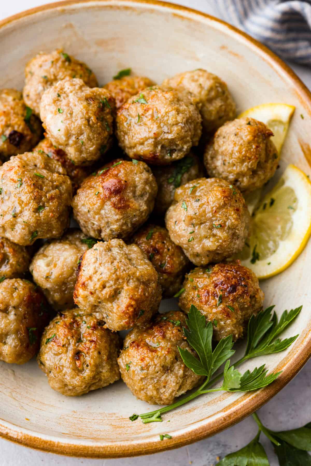 Baked Turkey Meatballs are tender, juicy, and perfectly seasoned. They're made with simple ingredients but big on flavor! These homemade meatballs are easy to make and healthy for the whole family! Close view of the meatballs served in a bowl garnished with parsley and lemon.