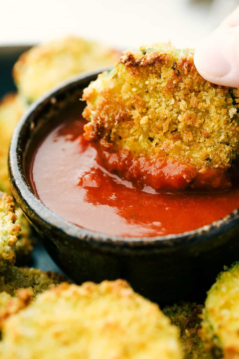 Air Fryer Parmesan Zucchini Chips are crunchy, savory bites of heaven! This is hands down one of the best ways to eat zucchini! Dipping an air fried zucchini chip in ketchup.