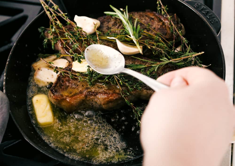 Skillet seared New York Steak is one of the best steaks you'll ever have!ย It's tender, juicy and full of flavor! Steak cooking in a black pan with butter and garlic.