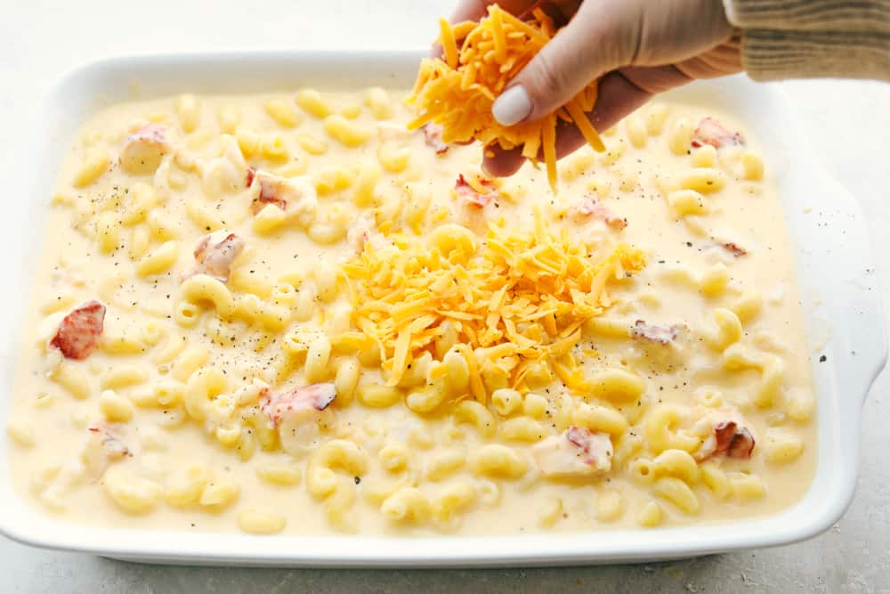 It's ooey and gooey, full of cheese and decadent rich lobster, this truly is an Incredible Lobster Mac and Cheese. Perfect for a special night or occasion, it's a macaroni and cheese that's sure to impress. Sprinkling cheddar cheese on a pan of lobster Mac and Cheese.