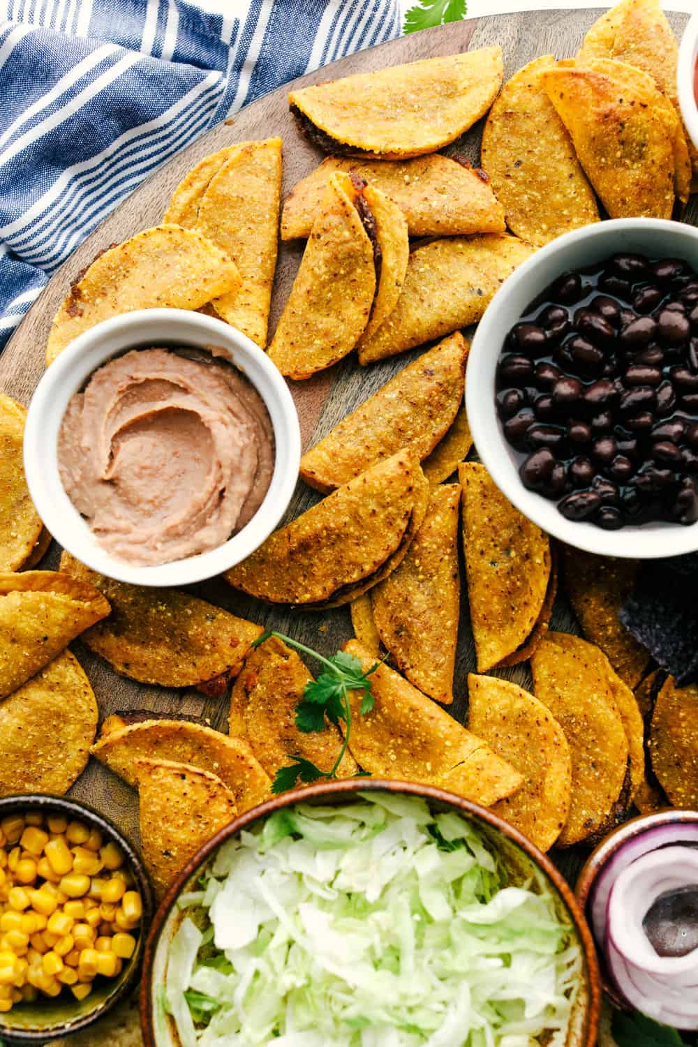This taco board is everything you need to have for the ultimate get together! It is the perfect combination! Taco board with tacos, bean dip, black beans, corn and lettuce in bowls on a board.