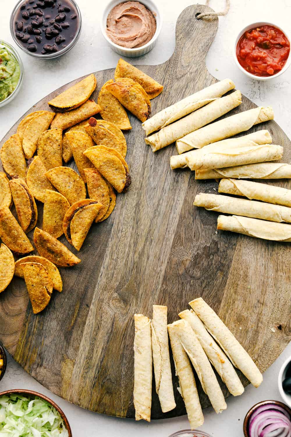 This taco board is everything you need to have for the ultimate get together! It is the perfect combination! A board with tacos and taquitos on it with bowls of dips and salsa around the edge.