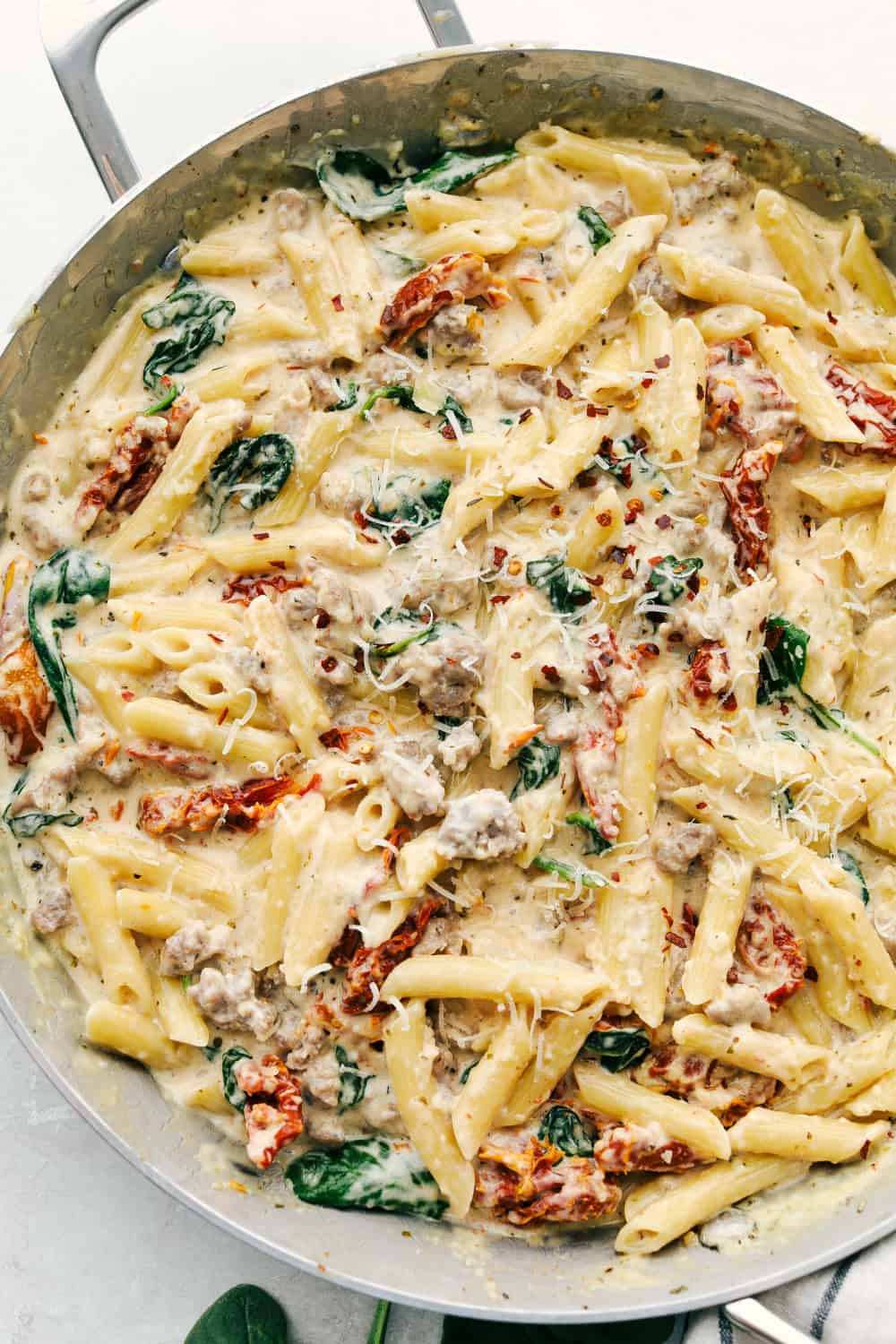 Creamy Tuscan sausage pasta is pretty much a one pan wonder you will want to cook over and over again!ย Perfect for a busy night, this is a hearty comforting dish that will truly satisfy. Creamy Tuscan Sausage Pasta in a pan garnished with parmesan cheese.