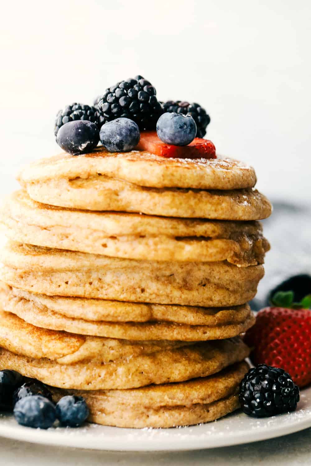 Fluffy Whole Wheat Pancakes are pillowy soft morsels of goodness! You are going to love this simple, easy, light but hearty pancake! A stack of whole wheat pancakes with berries on top.