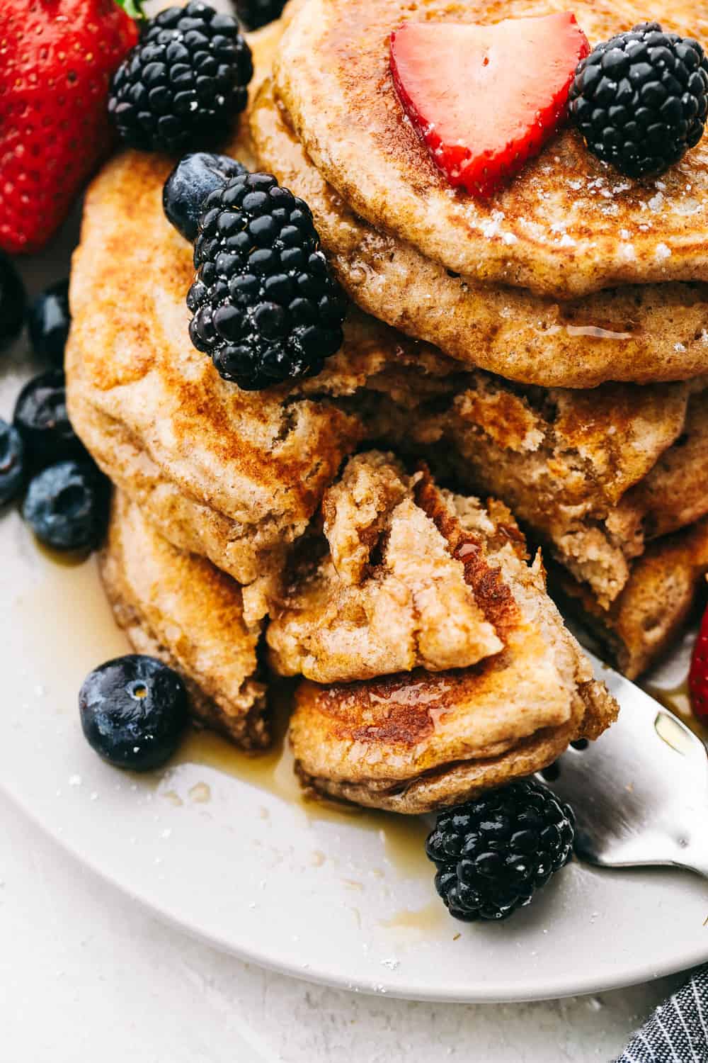 Fluffy Whole Wheat Pancakes are pillowy soft morsels of goodness! You are going to love this simple, easy, light but hearty pancake! Up close look at whole wheat pancakes cut into with berries and syrup.