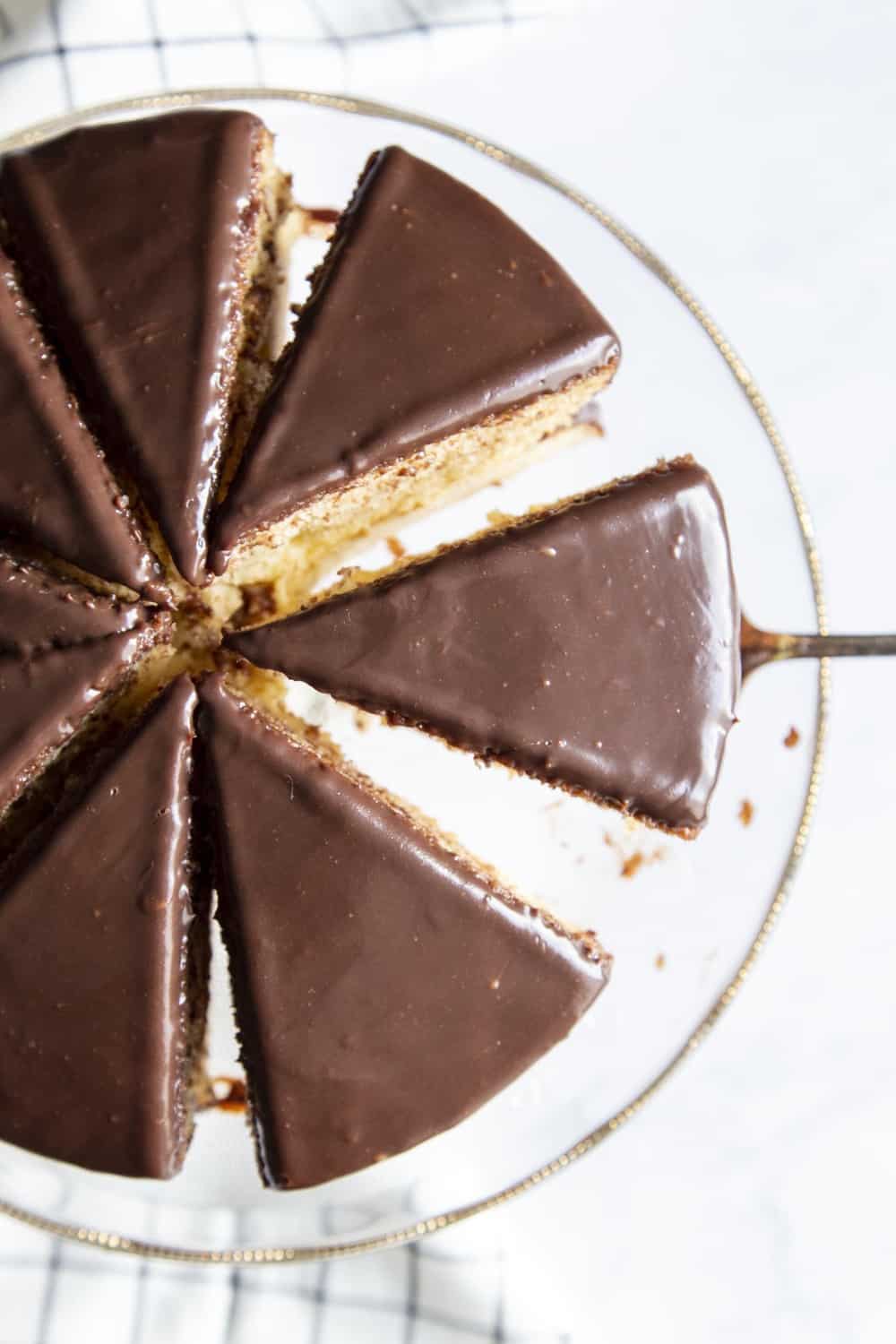 Boston Cream Cake is an American classic sure to win you over. It's a decadent light, fluffy cake, filled with a vanilla custard and topped with a rich chocolate ganache. Boston Cream Cake cut into slices.