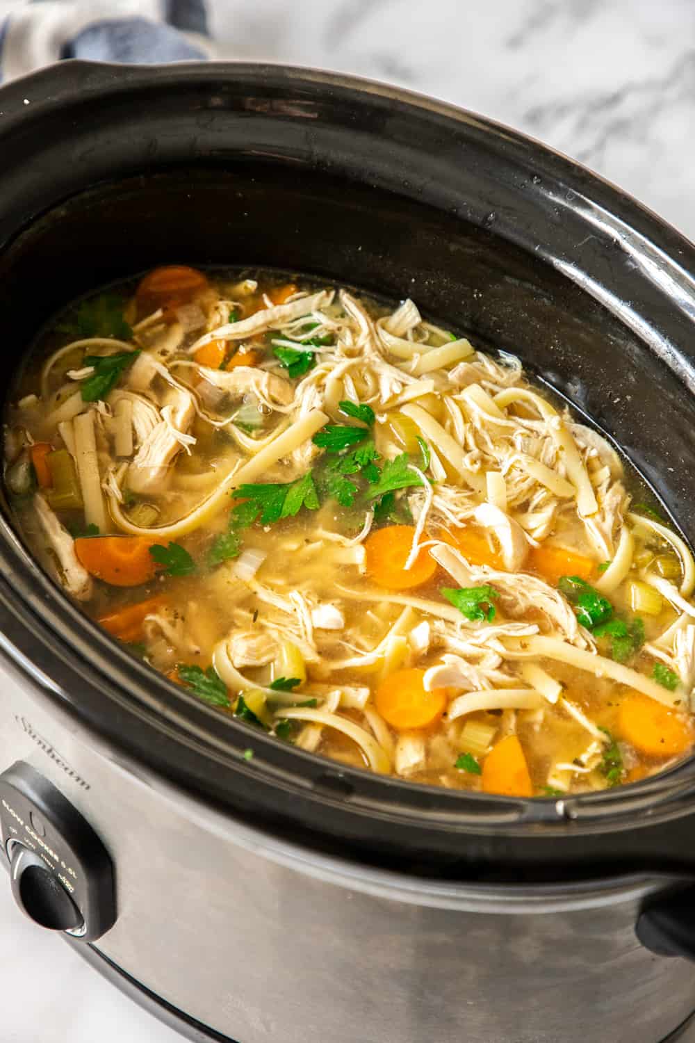 Comforting and hearty, this crockpot chicken noodle soup is so easy to make, and right in the slow cooker. Let the house fill with the most wonderful aroma knowing a cozy dinner is on the way! chicken noodle soup in the black bowl of a slow cooker