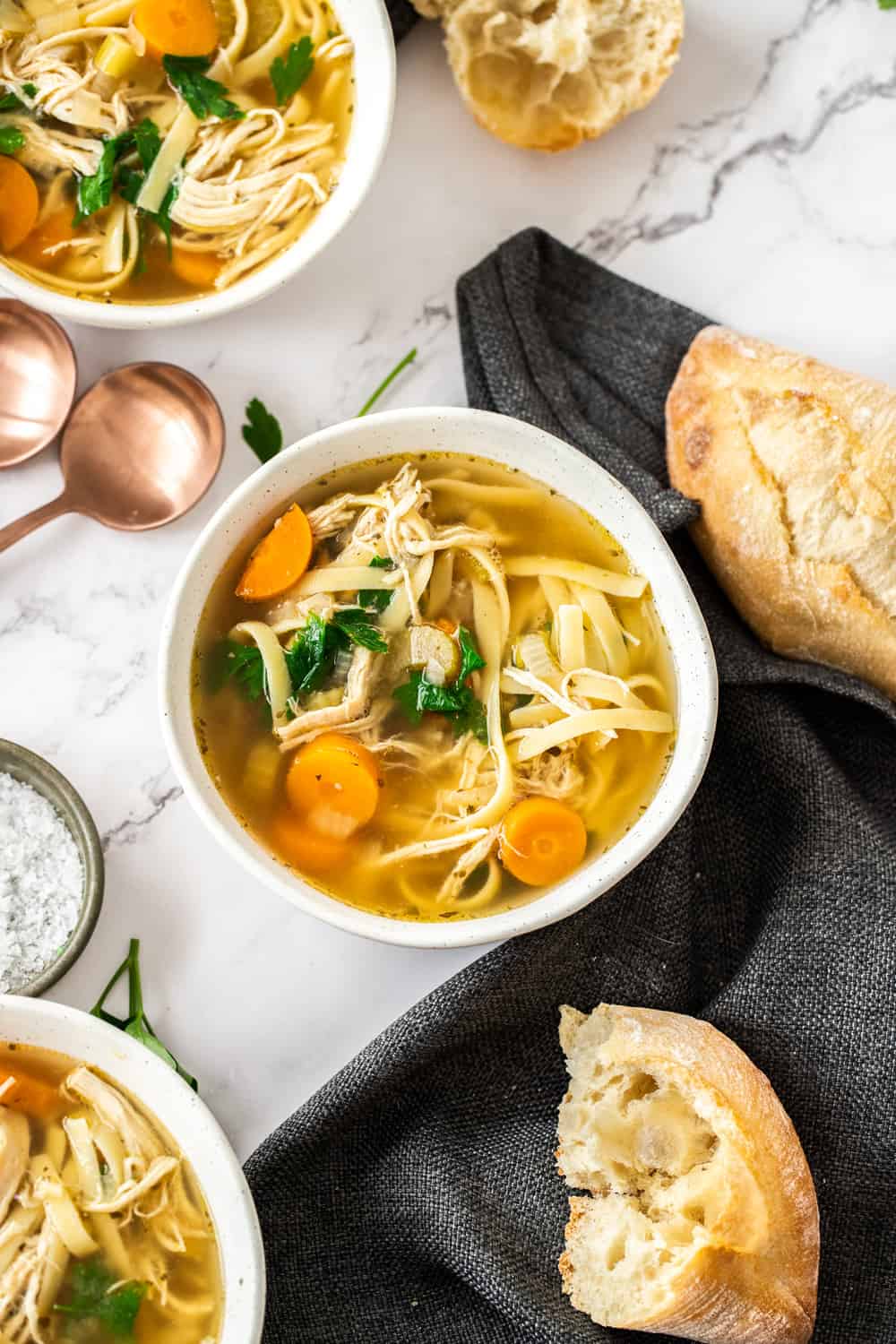 Comforting and hearty, this crockpot chicken noodle soup is so easy to make, and right in the slow cooker. Let the house fill with the most wonderful aroma knowing a cozy dinner is on the way! Top down view of a white bowl filled with chicken noodle soup.