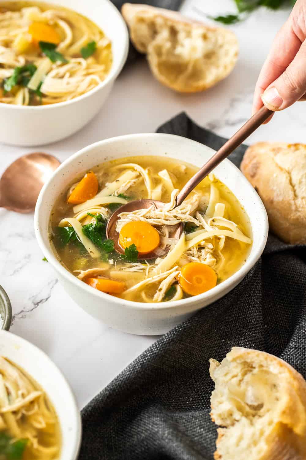 Comforting and hearty, this crockpot chicken noodle soup is so easy to make, and right in the slow cooker. Let the house fill with the most wonderful aroma knowing a cozy dinner is on the way! A white bowl filled with chicken noodle soup and a spoon digging in