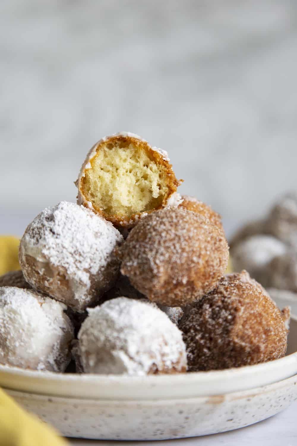 Donut Holes have to be the best part of making donuts. They are bite size and fun to eat! A tower of donut holes with one half eaten on top.