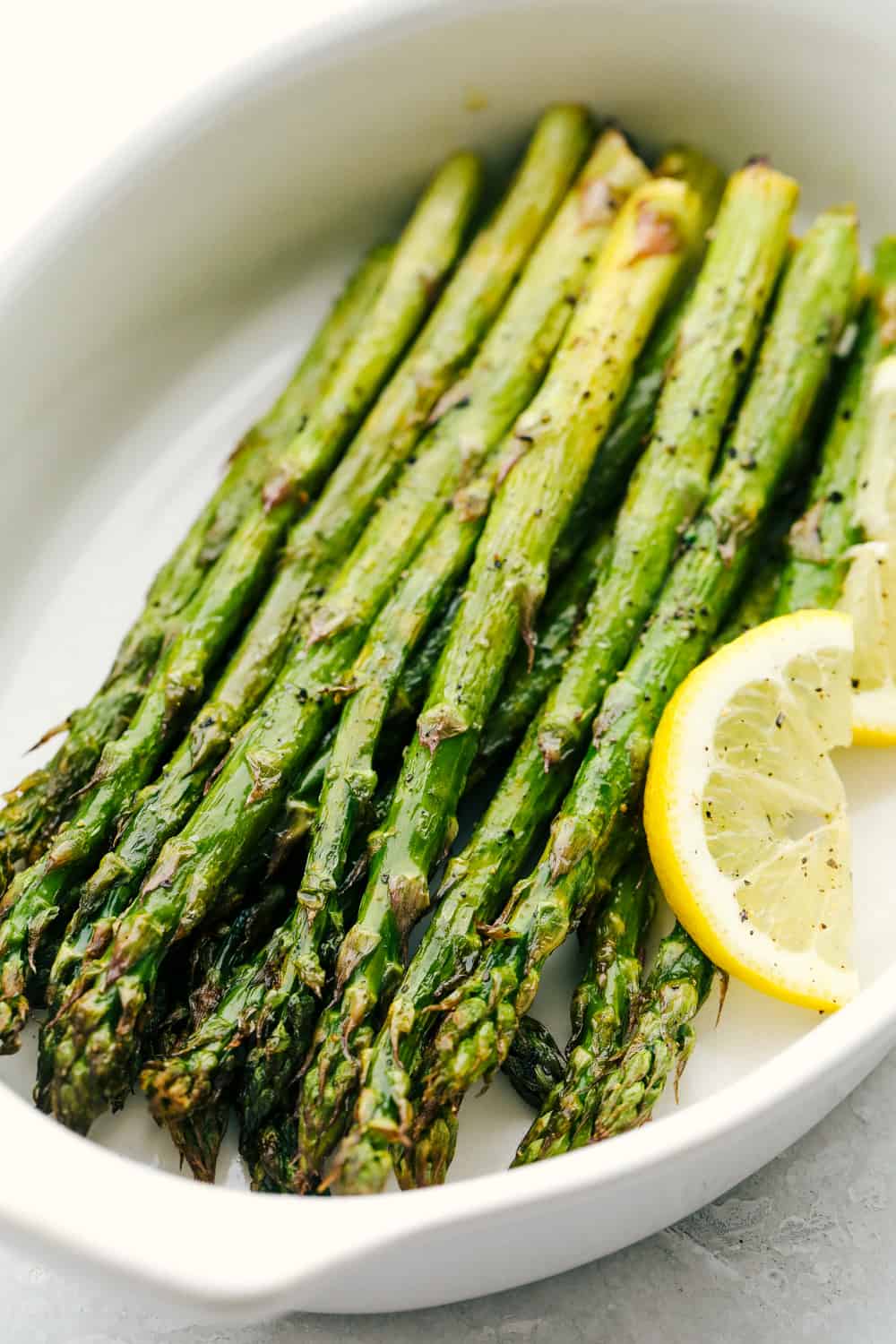 Air Fryer Asparagus is crisp, tender and delicious. This is hands down the best way to roast asparagus! Air fryer roasted asparagus in a white dish.