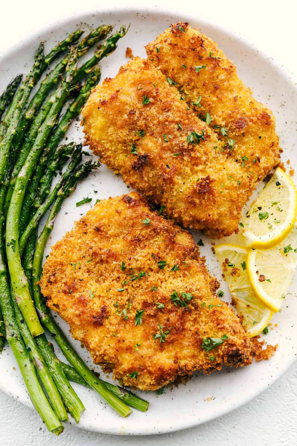 Air Fryer Cod will change the way you eat fish! Crispy golden outside and flakey tender inside, you are going to love this! Crispy parmesan air fryer cod with asparagus on a plate.