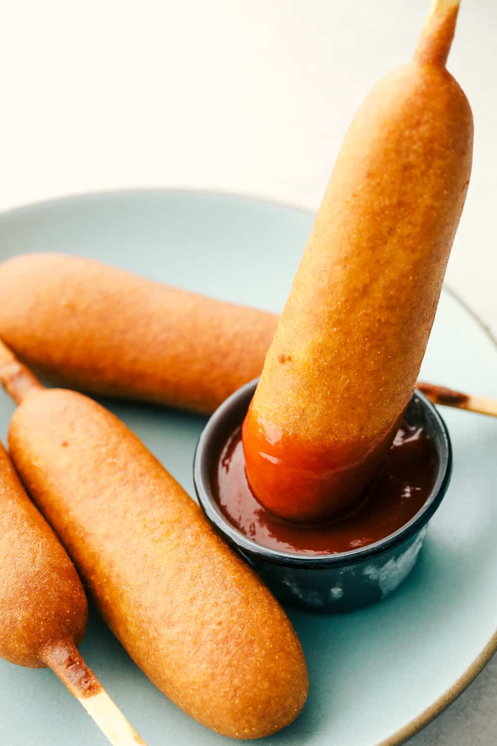 Air Fryer Corn Dogs is the best way to enjoy these fair favorites at home. Perfectly crispy tender outside and juicy on the inside! Dipping a corn dog in ketchup.