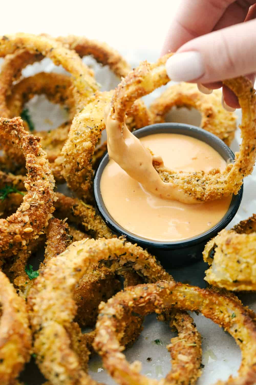 Crispy Air Fryer Onion Rings are going to be your new go to favorite. Golden, crunchy and cooked to perfection, these onion rings are so addicting! Dipping onion rings in dipping sauce for eating.