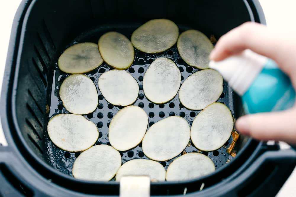 Air Fryer Potato Chips are a chip lovers dream come true! Now you can have all the chips, and none of the guilt! Spritzing sliced potatoes in air fryer with oil.