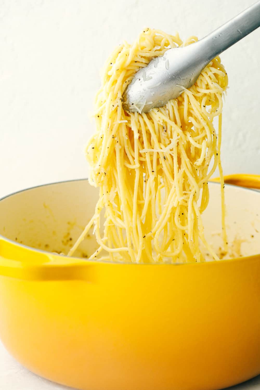 Cacio e Pepe is a quick cheesy dish that's sure to hit the spot. This is a comfort food that's easy and insanely delicious! Hot noodles with Pecorino Romano Cheese and seasoning being lifted out of the pot with tongs.