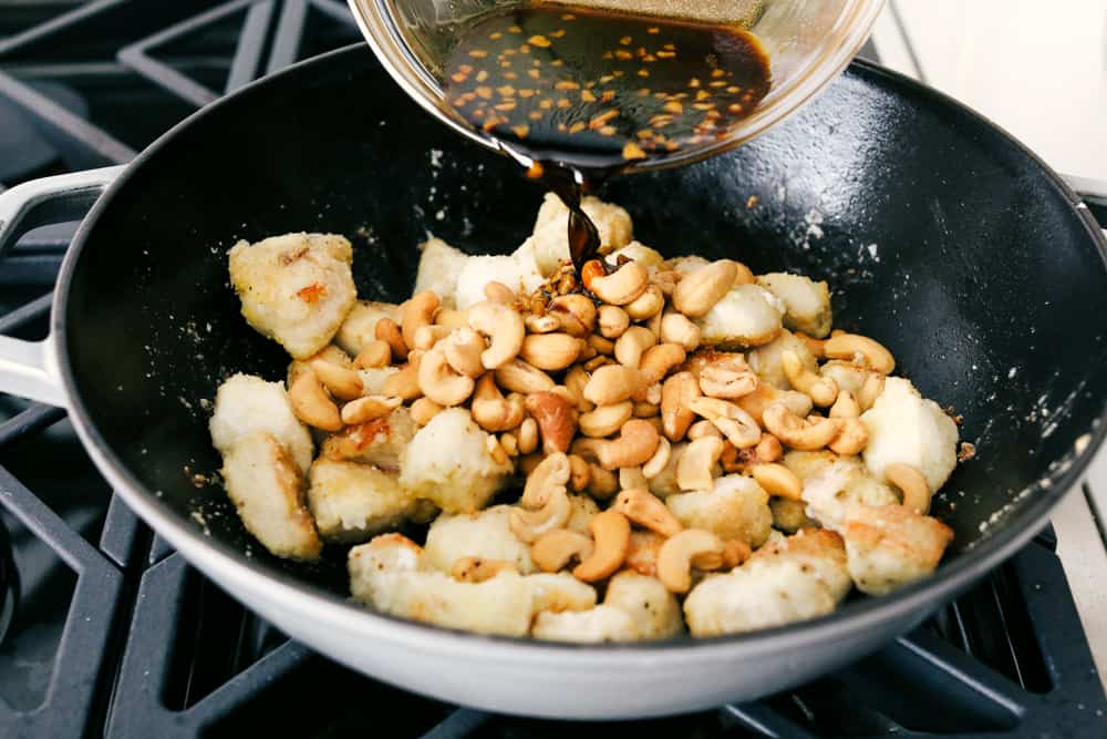 Someone pouring sauce over cashew mixture in a wok. 